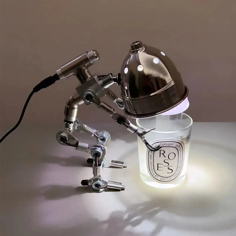 Silver metallic robot-shaped decorative desk lamp with internal LED glow on a wooden surface.