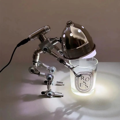 Silver copper robot-shaped desk lamp with custom graphic on a wooden shelf.