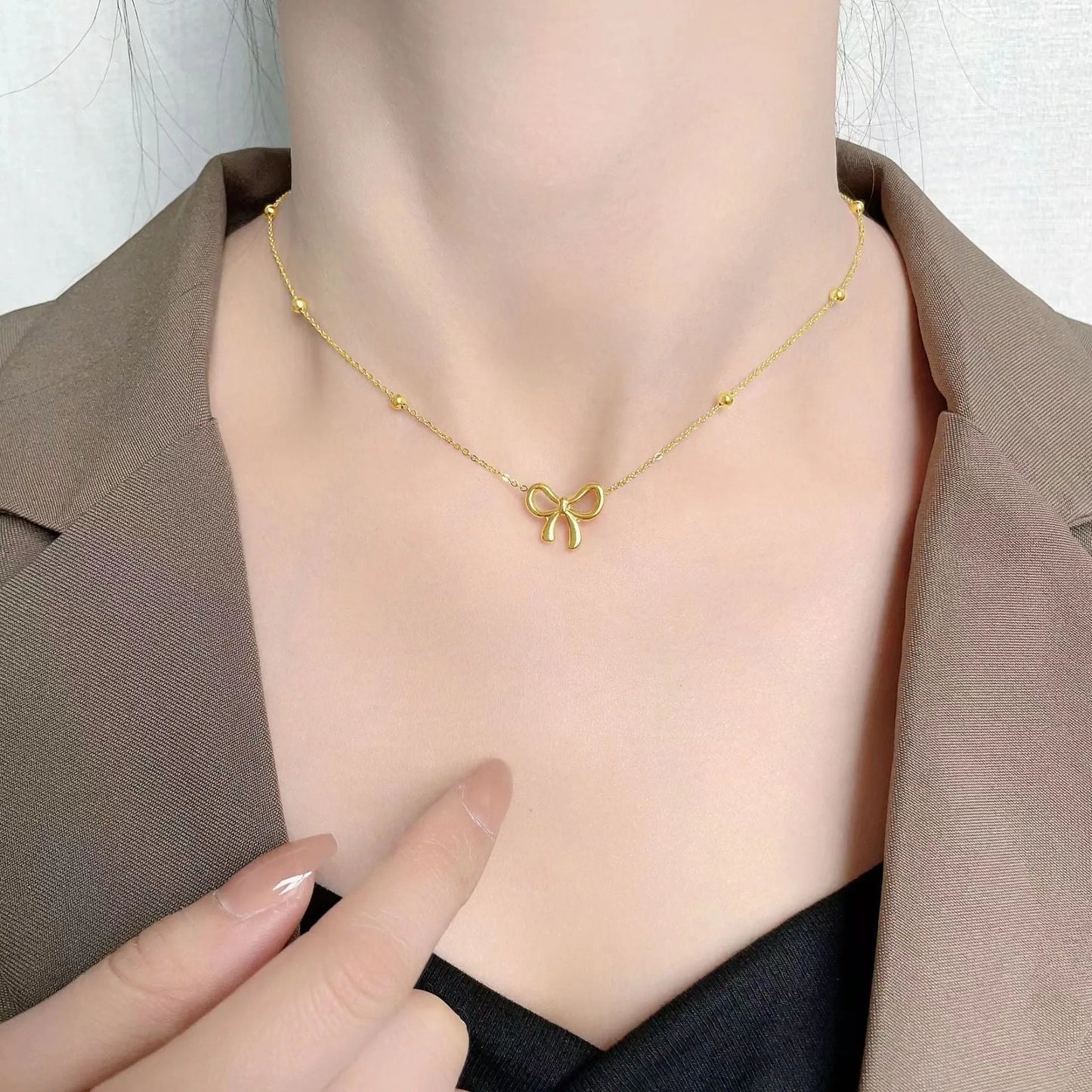 Gold electroplated bow pendant on an adjustable titanium steel cross chain necklace for women.