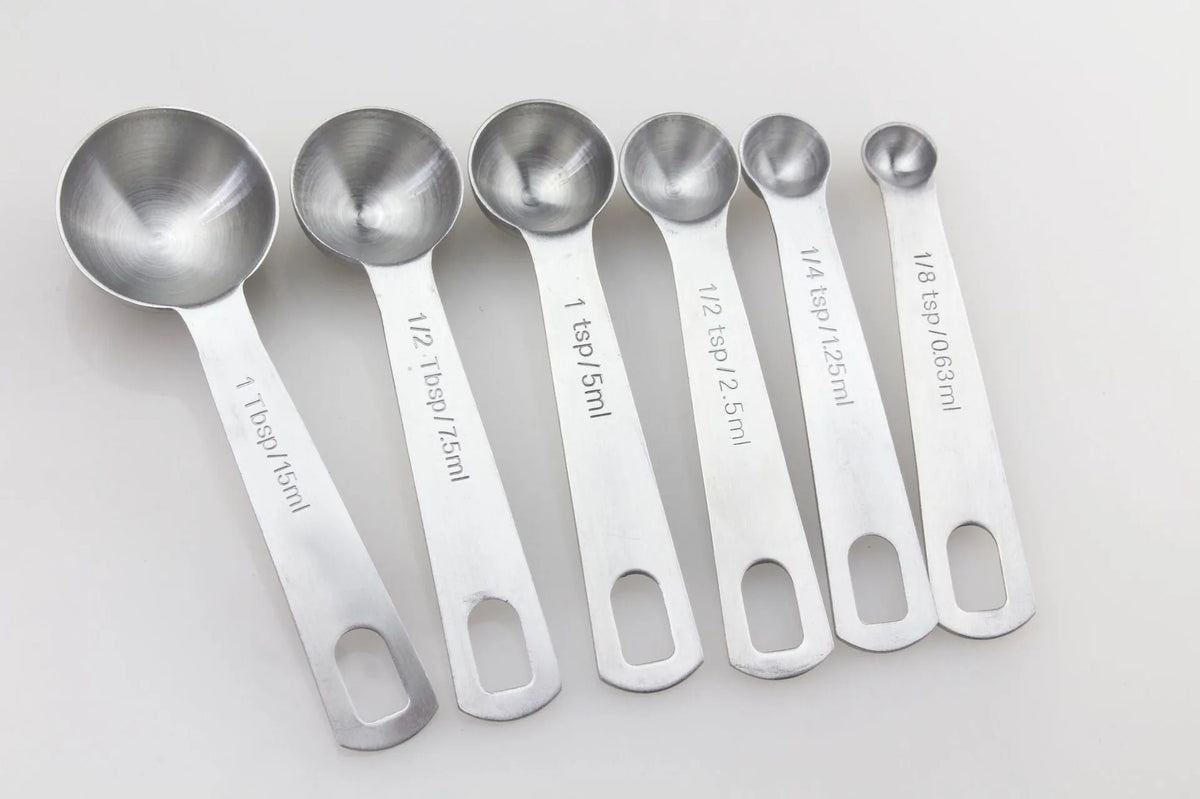 Six stainless steel measuring spoons with engraved markings and D-shape ring, sizes 1/8 tsp to 1 Tbsp