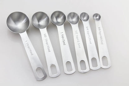 Six stainless steel measuring spoons with engraved markings and D-shape ring, sizes 1/8 tsp to 1 Tbsp