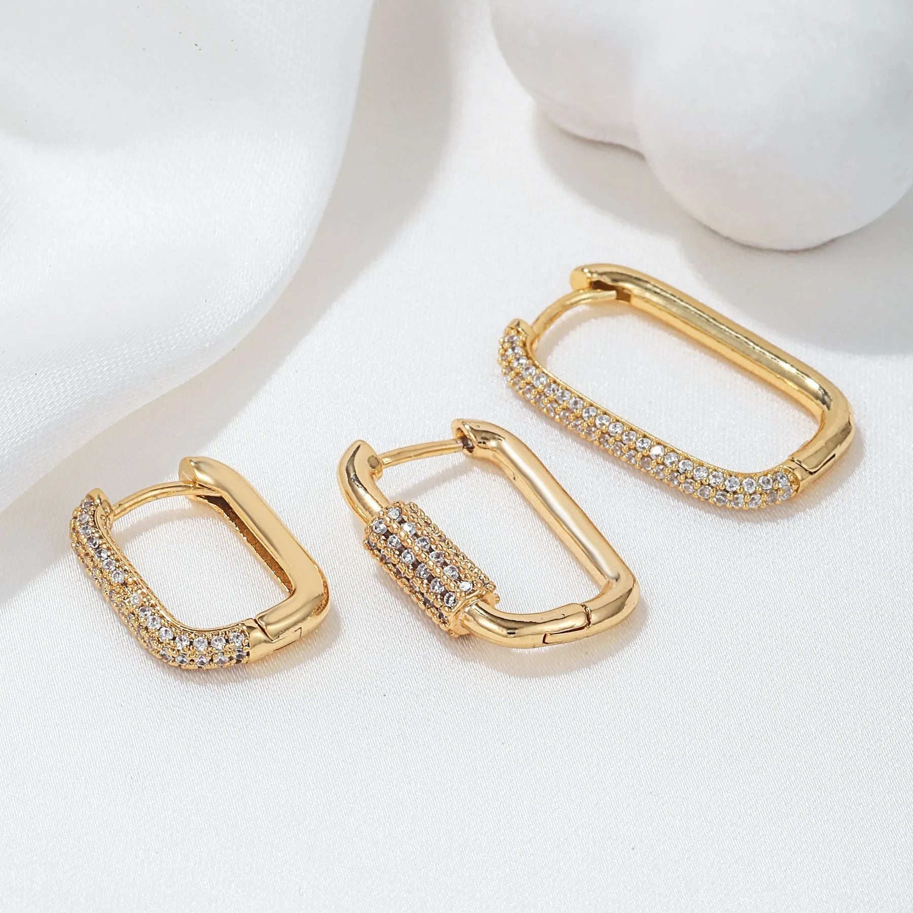 Three geometric copper ear clips with micro inlaid zircon in gold and white tones on a grey background.