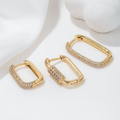 Three geometric copper ear clips with micro inlaid zircon in gold and white tones on a grey background.