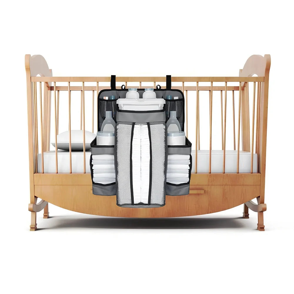 Grey baby nappy organiser attached to crib rail with Velcro straps, showing storage compartments for nappies and essentials