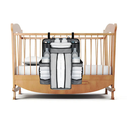 Grey baby nappy organiser attached to crib rail with Velcro straps, showing storage compartments for nappies and essentials