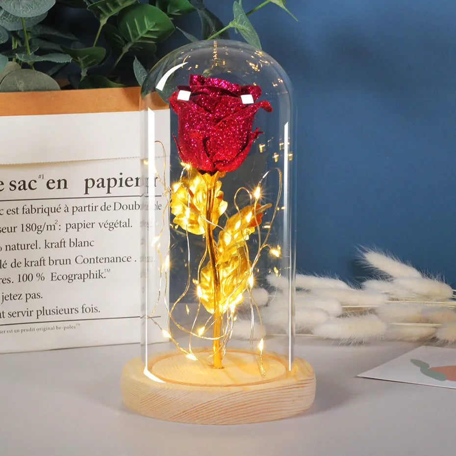 Red eternal rose flower arrangement with LED lights inside a glass dome on a table.
