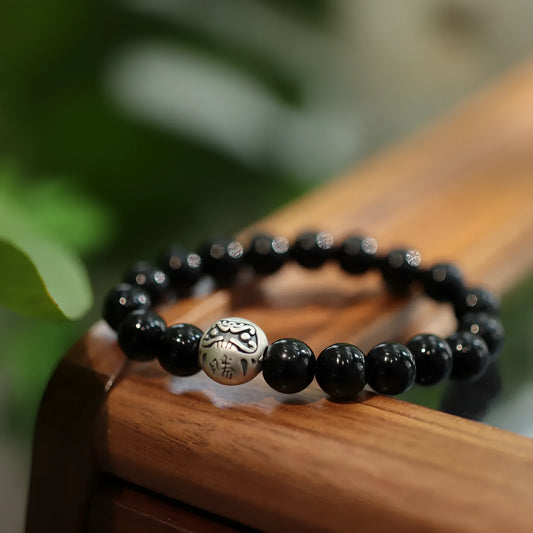 A bracelet with large black agate beads and a sterling silver clasp on a wrist.