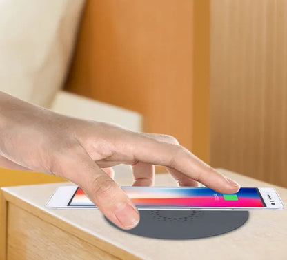 Round wireless charging unit for recessed installation in desks and tables, shown next to a smartphone.