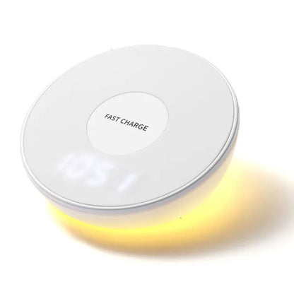 White wireless charging stand with digital clock display, showing time, next to a mobile phone on its angled charging platform.