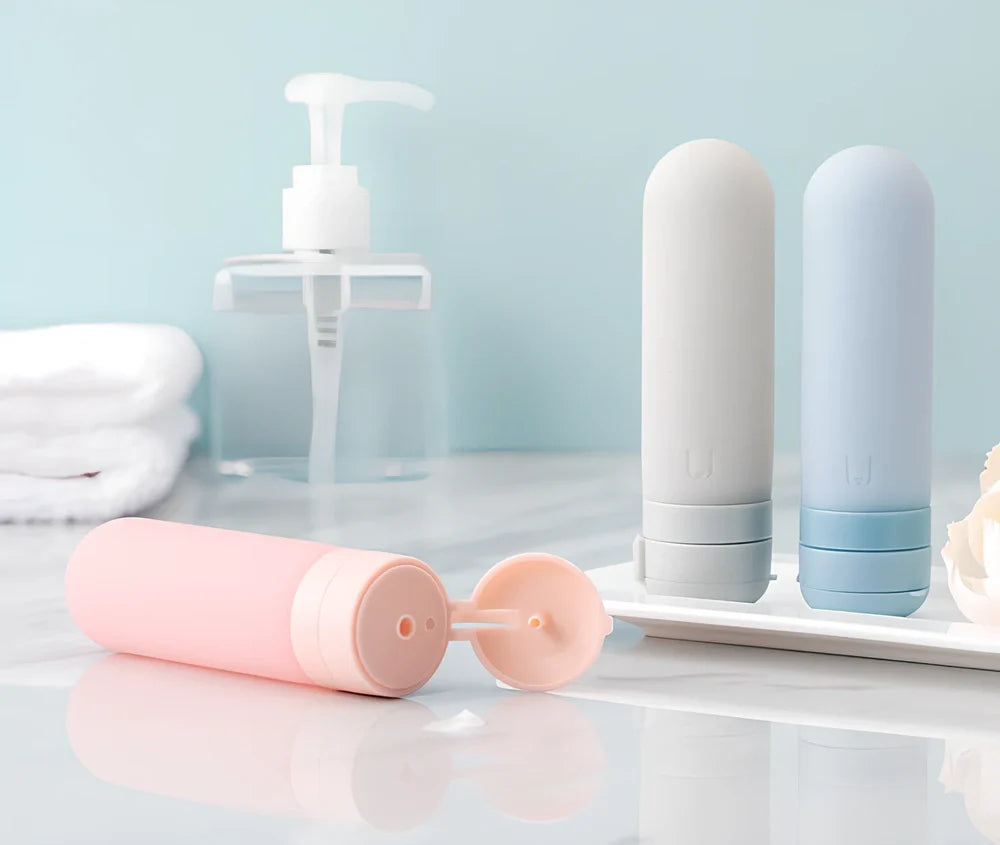 Set of three silicone travel bottles in light grey, pink, and blue colours with screw caps