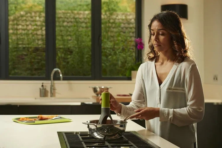 Uutensil Stirr automatic electric kitchen mixer device in green, shown next to a saucepan.