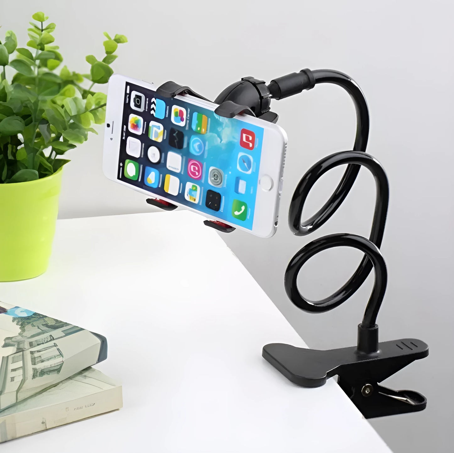 Black flexible arm mobile phone holder with V-clip gripping a smartphone, extended to 70cm on a bedside table.
