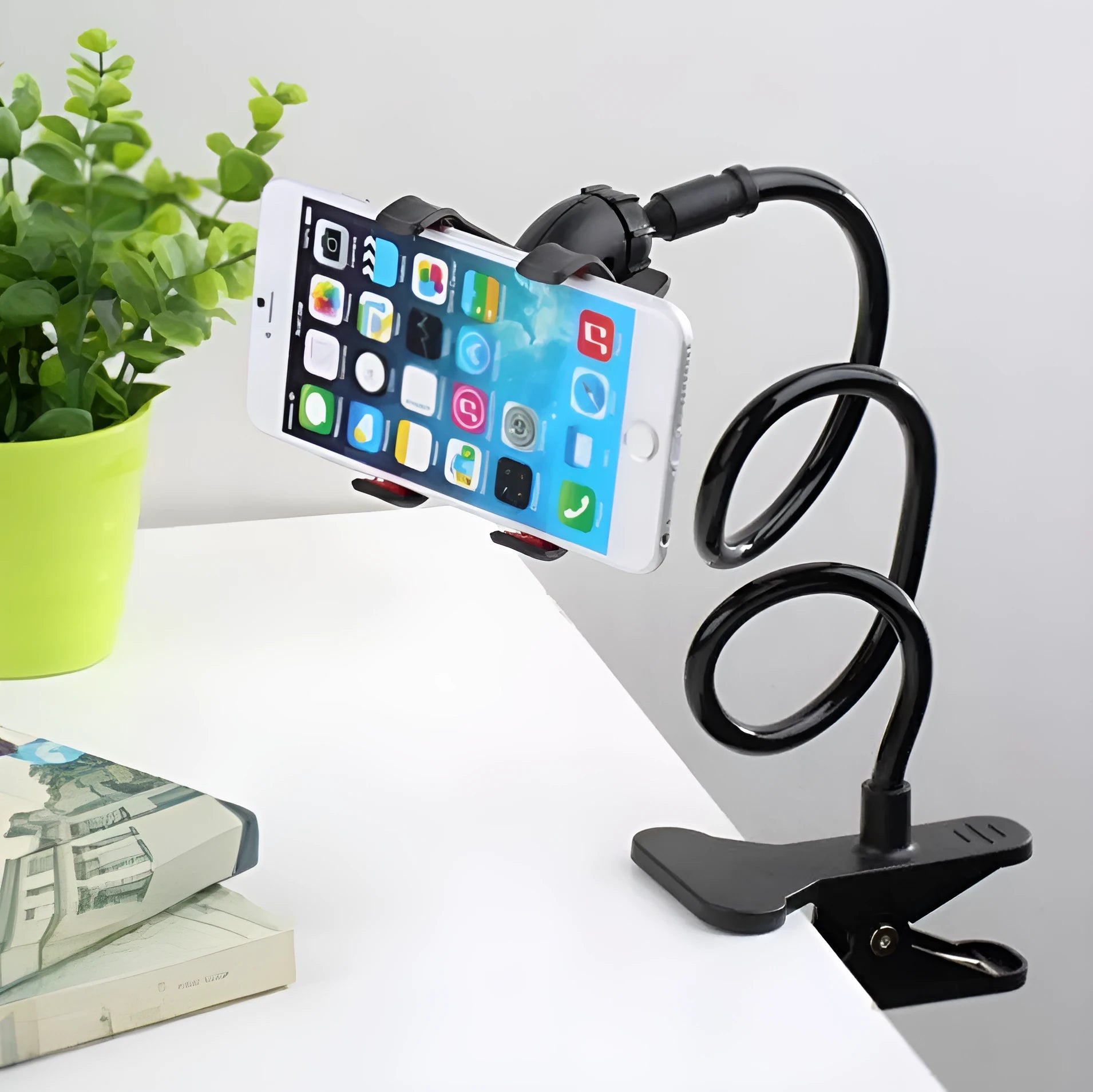 Black flexible arm mobile phone holder with V-clip gripping a smartphone, extended to 70cm on a bedside table.