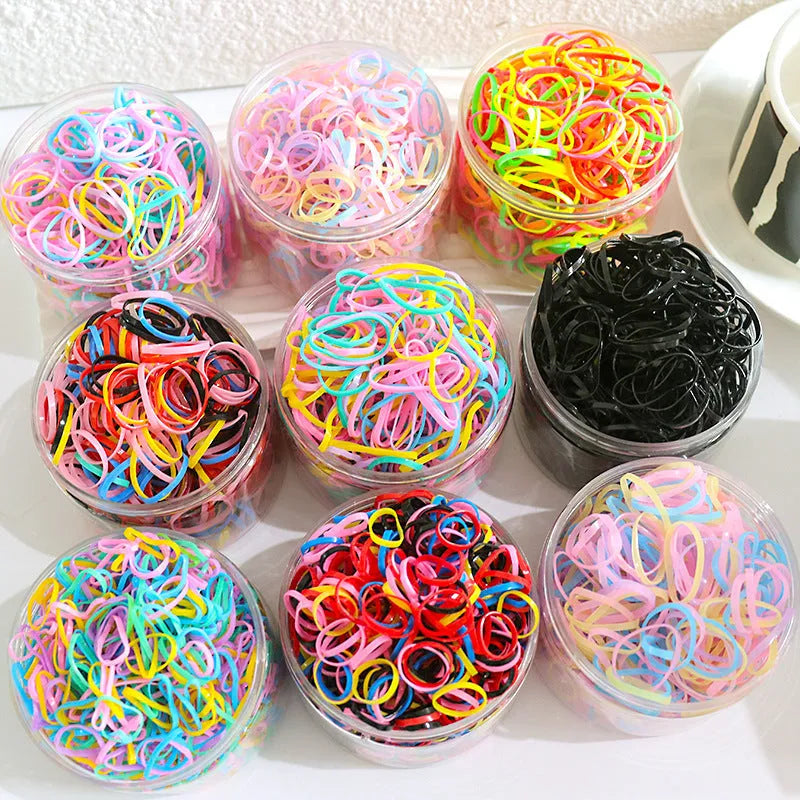 Multicoloured assortment of thin TPU elastic hair bands for babies and children in a reusable plastic container.