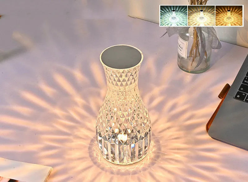 Transparent vase-shaped crystal table lamp with remote control on a wooden bedside table.