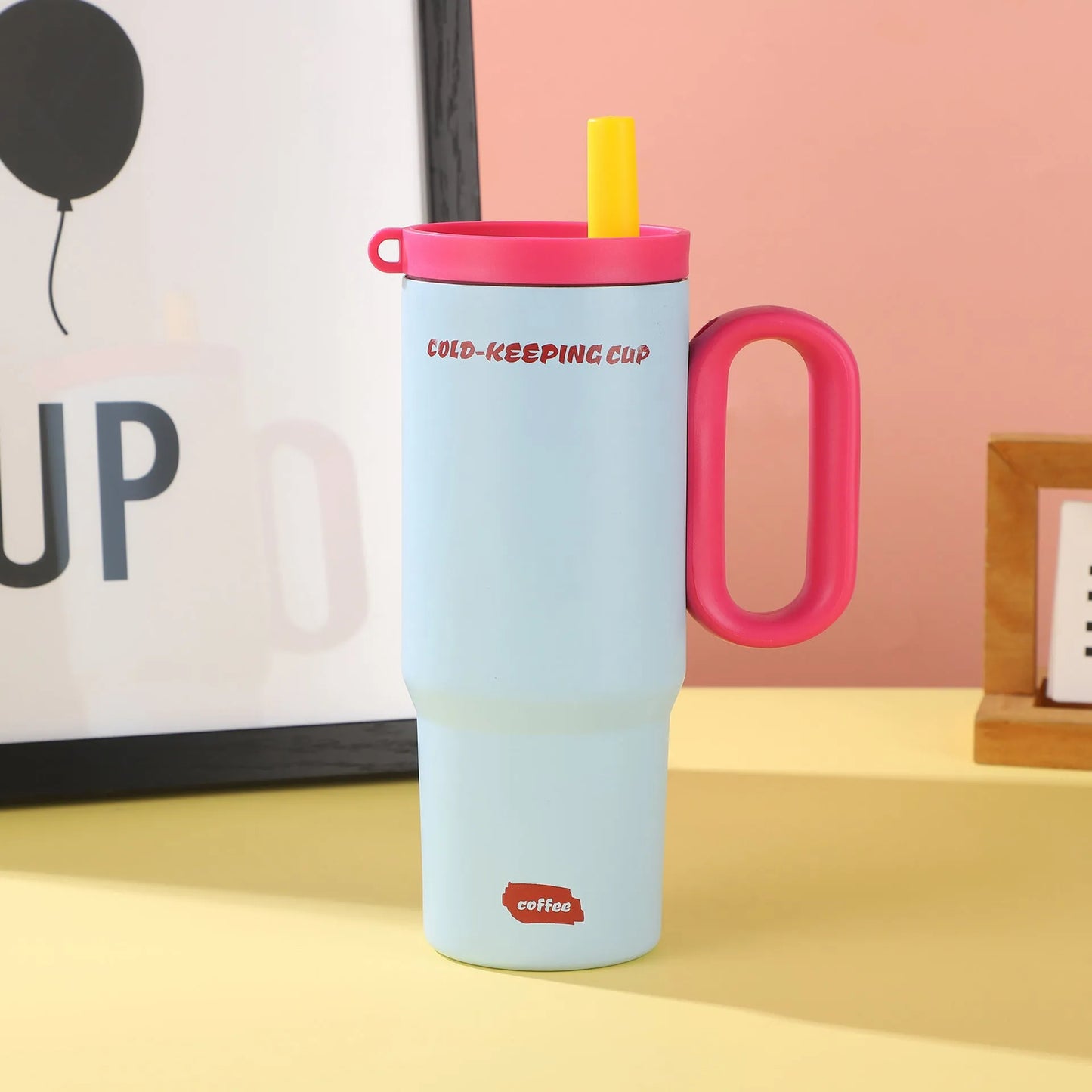 Large pink insulated straw cup with a black handle and push-button lid on a wooden table