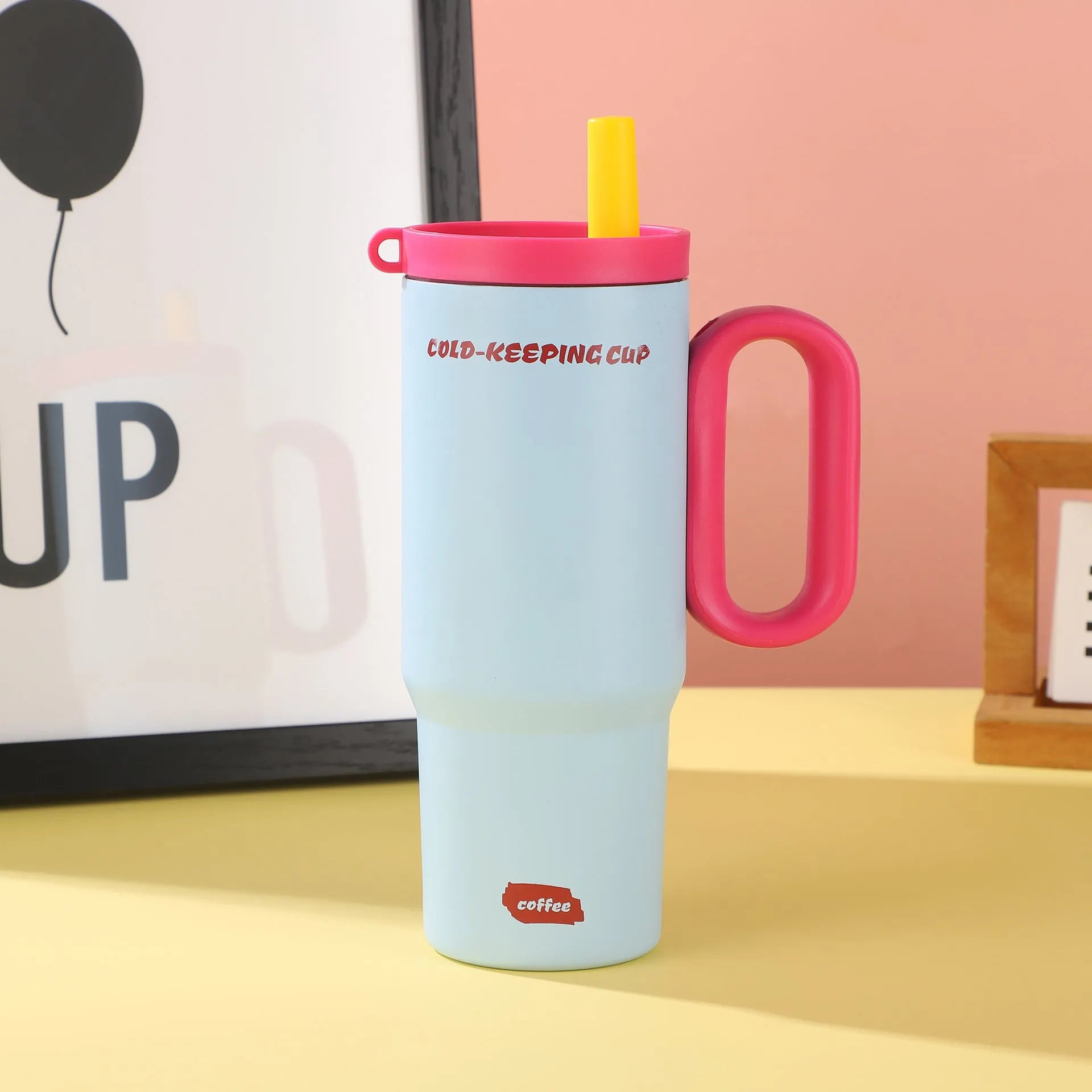 Large pink insulated straw cup with a black handle and push-button lid on a wooden table