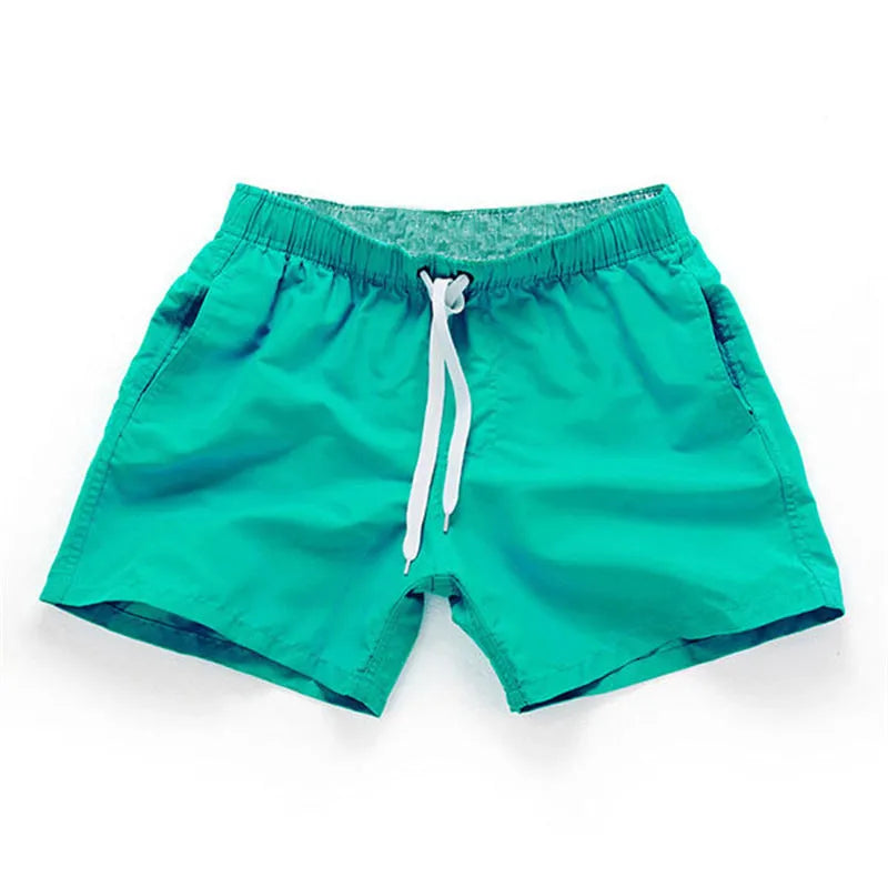 Man wearing straight-leg polyester beach shorts in a bright colour on the sand.