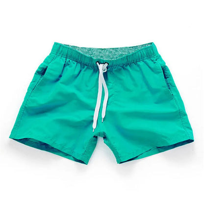 Man wearing straight-leg polyester beach shorts in a bright colour on the sand.