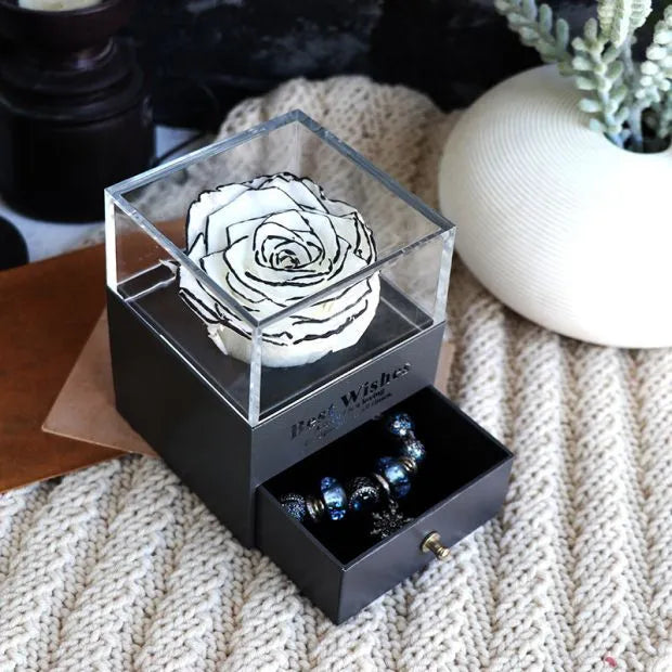 Blue and pink eternal flower gift box with roses and carnations on a table.