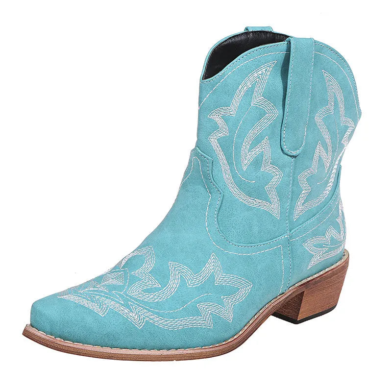 Women's brown embroidered ankle cowboy boots with a low wedge heel and pointed toe on a wooden floor.