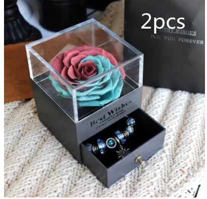 Blue and pink eternal flower gift box with roses and carnations on a table.