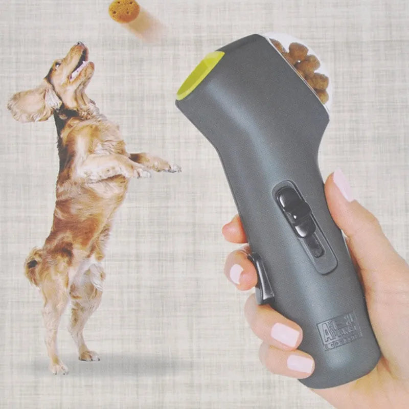 Grey plastic pet snack catapult launcher toy with ergonomic handle, shown with treats.