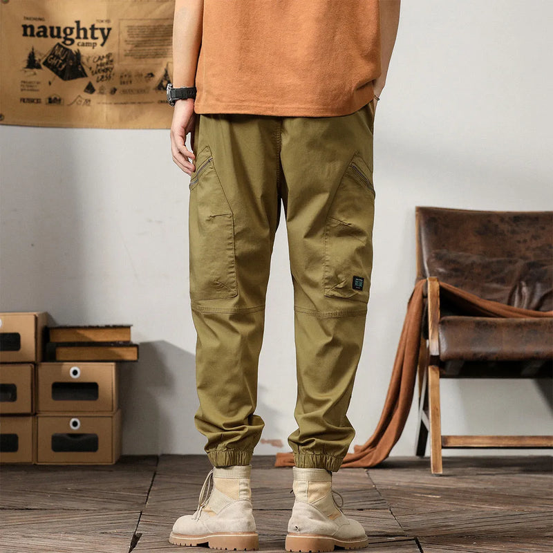 Men's casual trousers in mid-waist harem style with tapered ankle banding and zip fly placket, available in khaki, peacock green, coffee, and black cotton fabric with micro-elastic comfort for everyday leisure wear