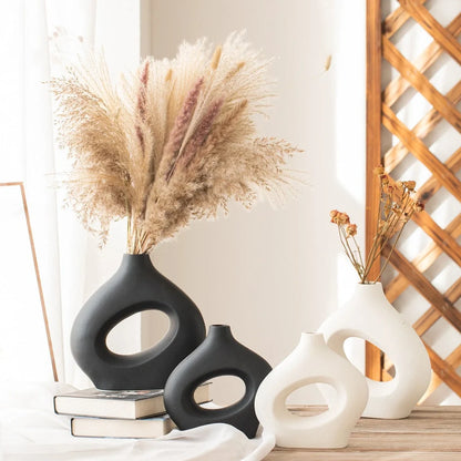 White ceramic circle vase with hand-painted coloured glaze on wooden table with dried flowers