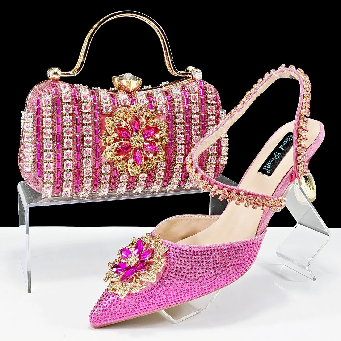 Women's black high-heel ankle strap shoes with floral rhinestone buckle and matching clutch bag on a neutral background