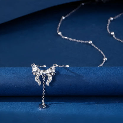 Close-up of a silver heart and bow pendant on an adjustable O-ring chain, resting on a collarbone.