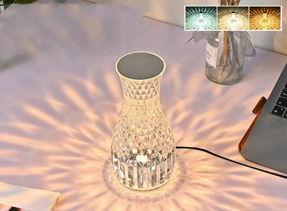 Transparent vase-shaped crystal table lamp with remote control on a wooden bedside table.