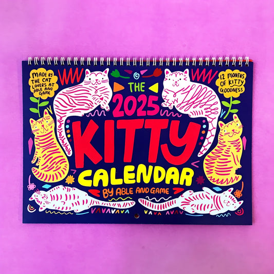 Cat-themed paper wall calendar for 2024 or 2025 year, showing monthly grid with feline artwork.