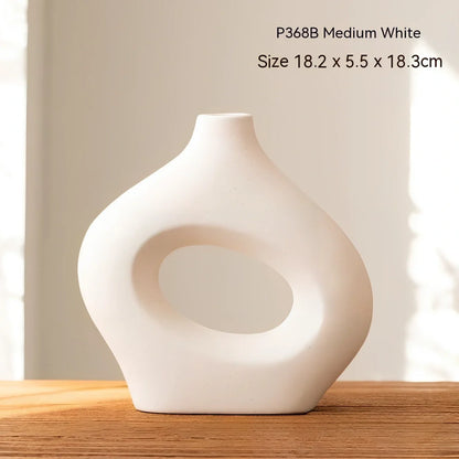 White ceramic circle vase with hand-painted coloured glaze on wooden table with dried flowers