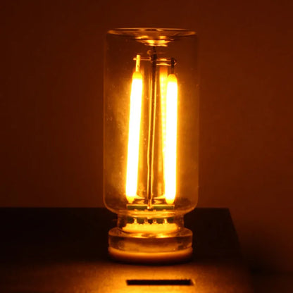 Small transparent glass USB touch night lamp with warm white light on a surface.
