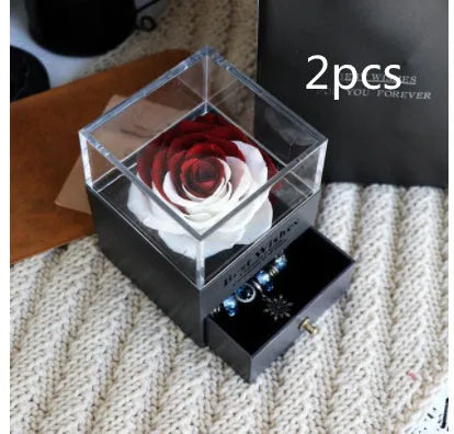 Blue and pink eternal flower gift box with roses and carnations on a table.