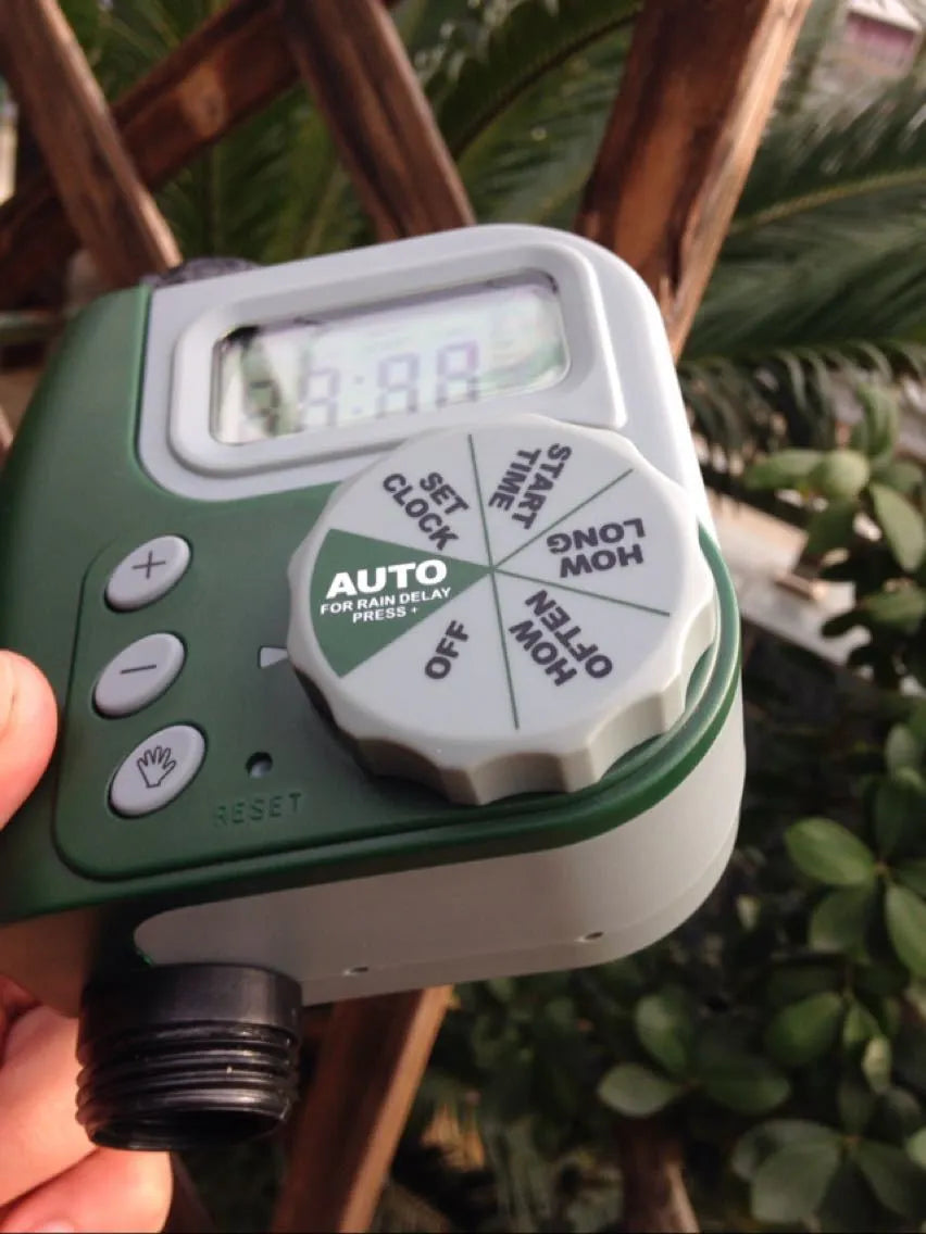 Green digital garden hose timer with LCD screen and dual hose outlets.
