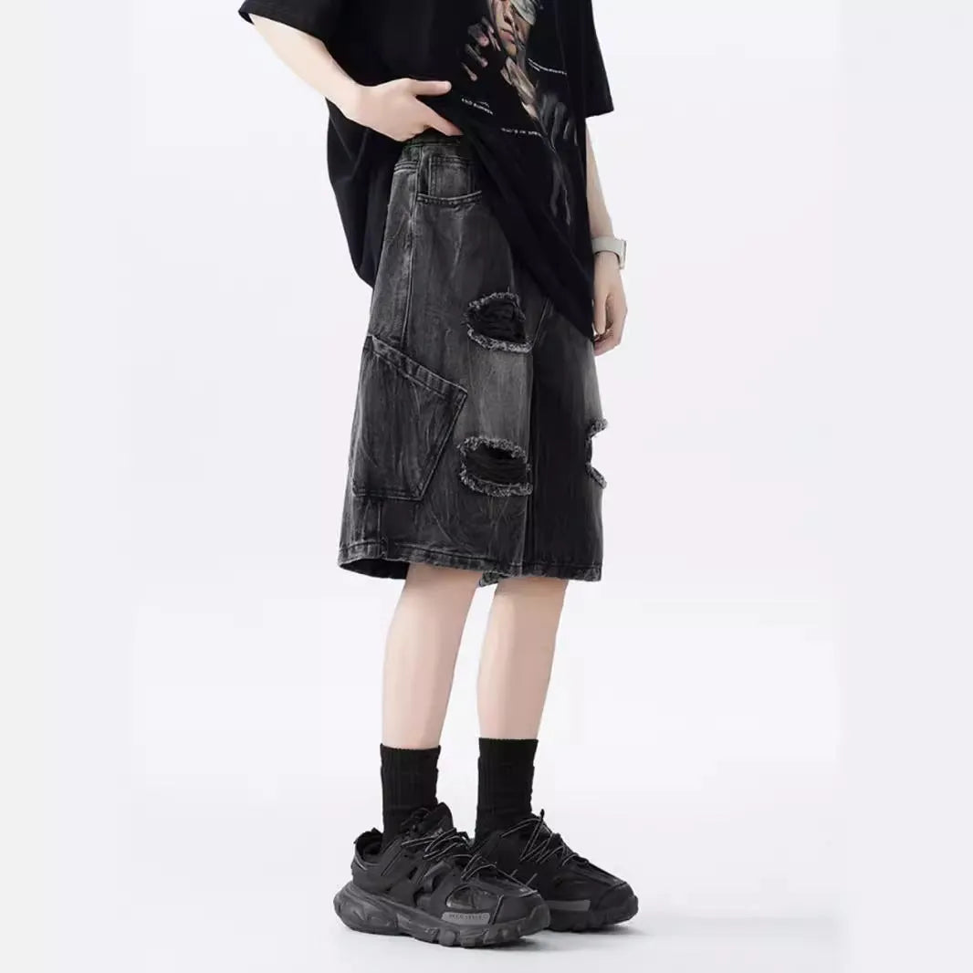 Man wearing loose fit black ripped denim shorts with distressed detailing and a washed vintage finish.