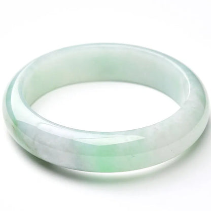 Light green solid jade bracelet on a wrist, showing its simple loop design and natural stone colour.