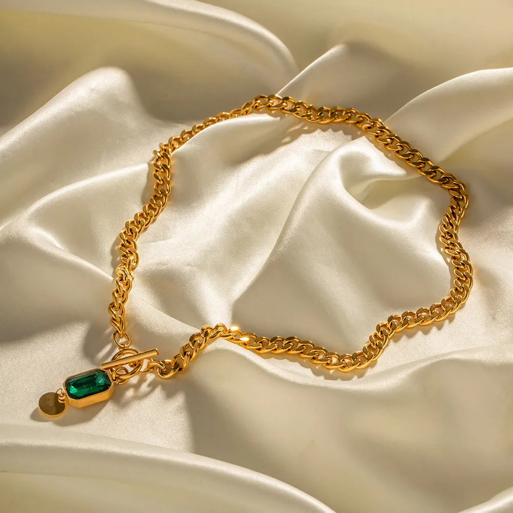 Gold geometric pendant necklace with emerald green zircon on a textured Cuban link chain.