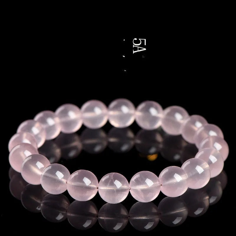 A polished natural starlight crystal round bead bracelet in pink, showing different size options on a wrist.