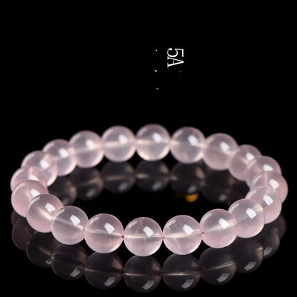 A polished natural starlight crystal round bead bracelet in pink, showing different size options on a wrist.