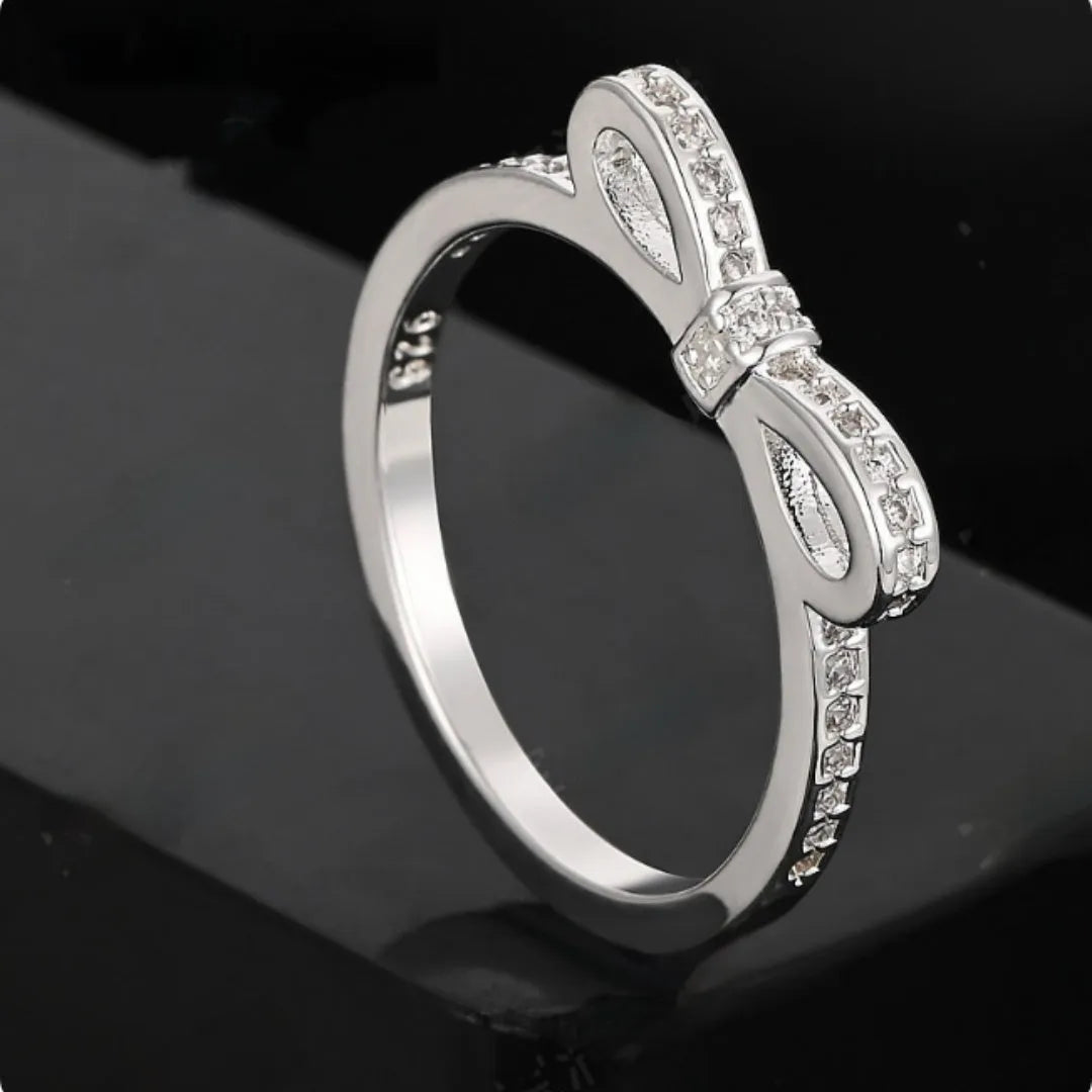 Silver bow-shaped ring with zircon crystal accents on finger, showing electroplated finish and detailed bow design