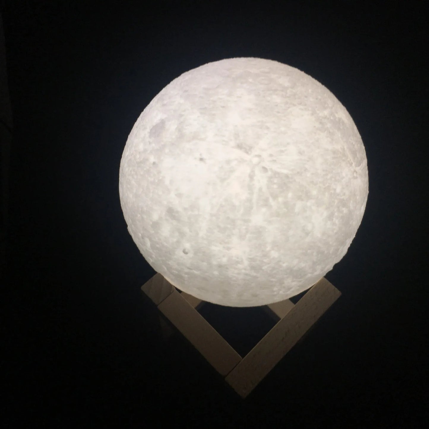 3D printed white moon lamp glowing on a wooden stand, showing detailed crater texture on its surface.