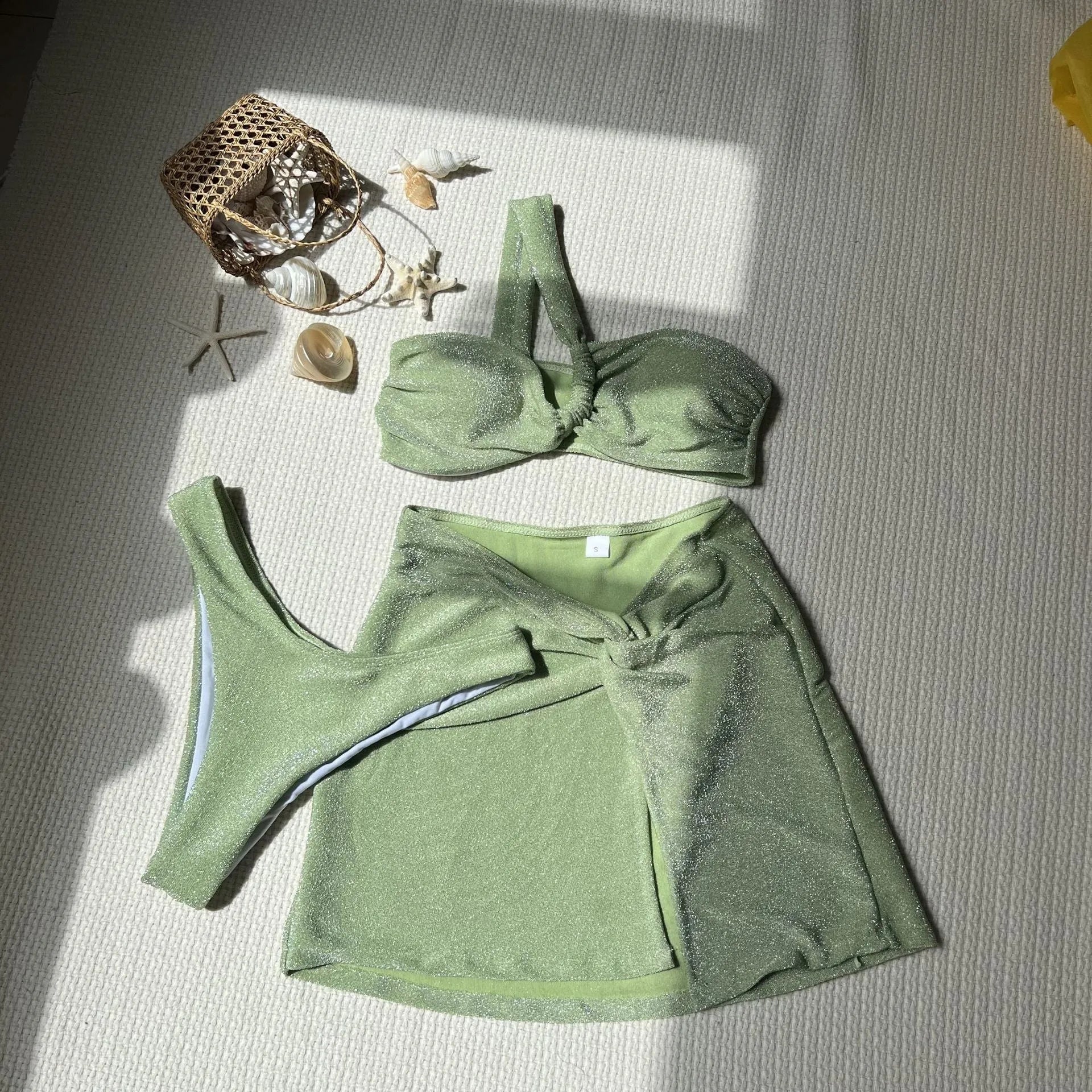 Women's one-shoulder glossy polyester swimsuit set in light green, with matching pants and skirt