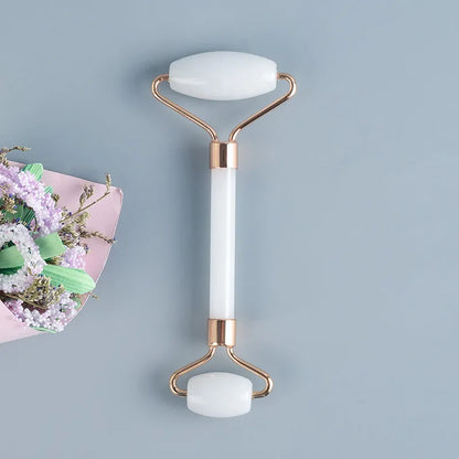 White jade facial roller with double heads and matching scraping board on dark surface