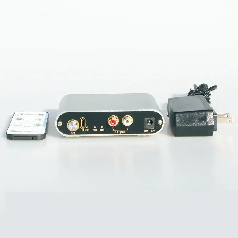 Silver aluminium audio source switch selector unit with infrared remote control on a black surface.