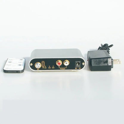 Silver aluminium audio source switch selector unit with infrared remote control on a black surface.