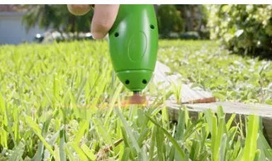 Cordless handheld lawn trimmer with green housing, extension pole, debris shield, and pack of zip ties on a garden lawn.
