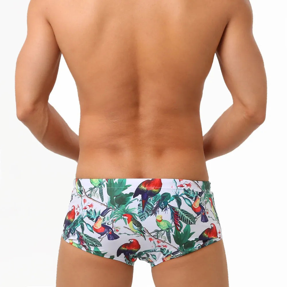 Men's blue swimming trunks with a detailed floral and bird print pattern, shown in a brief style.